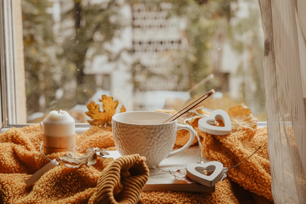 An image showing a mug on a blanket, surrounded by fairy lights next to a candle and autumn leaves.